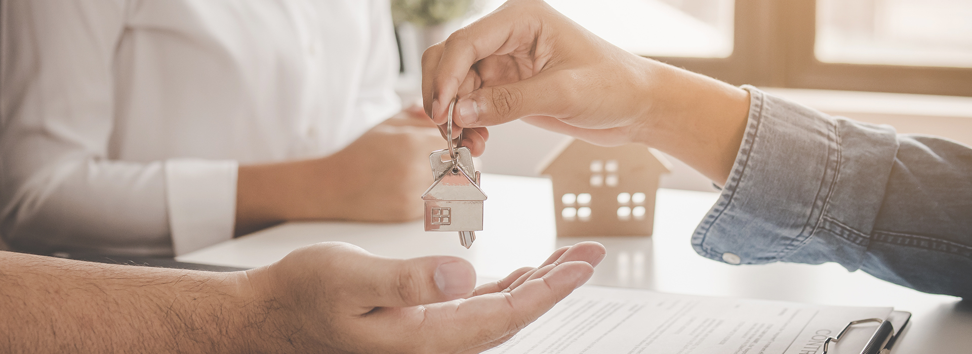 close up of hands handing off keys with a house keychain